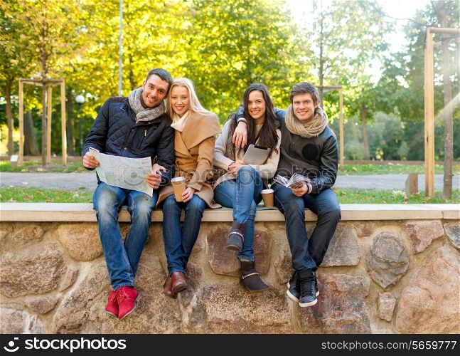 travel, vacation, people, tourism and friendship concept - group of smiling friends sitting with tablet pc computer map and hot drinks in park