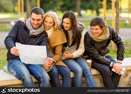 travel, vacation, people, tourism and friendship concept - group of smiling friends sitting with tablet pc computer city guide and map in park