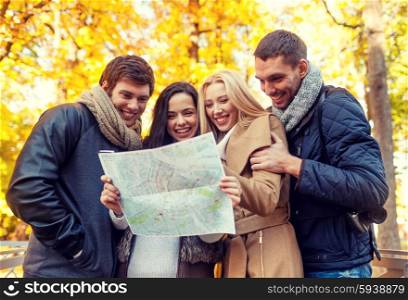 travel, vacation, people, tourism and friendship concept - group of smiling friends looking to map in city park