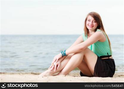 Travel, vacation, summertime, holiday concept. Happy smiling woman wearing short colorful dress sitting on beach with sea in background.. Happy woman sitting on beach near sea