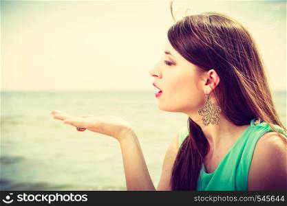 Travel, vacation, summertime, holiday concept. Profile portrait of happy woman sending air kiss wearing blue top, sea in background.. Woman sending air kiss on beach near sea