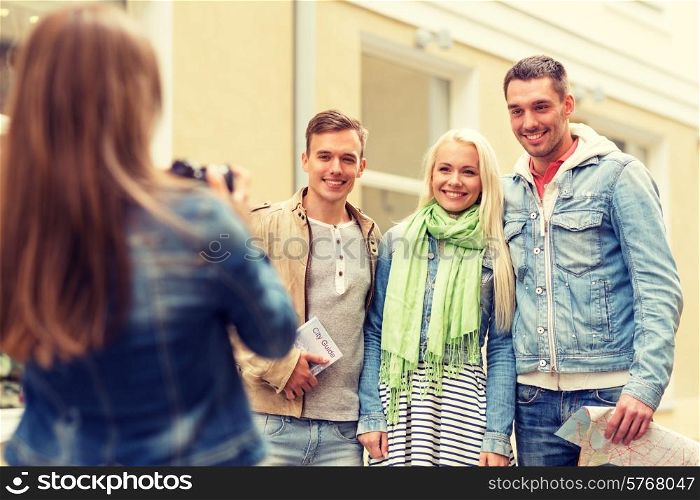 travel, vacation, technology and friendship concept - girl picturing group of friends with map and city guide in city