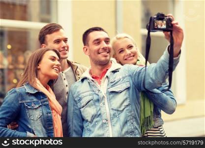 travel, vacation, technology and friendship concept - group of smiling friends making selfie with digital camera outdoors