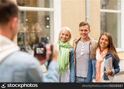 travel, vacation, technology and friendship concept - guy picturing group of friends with map in city