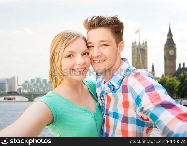 travel, vacation, technology and friendship concept - happy couple taking selfie over big ben and thames river in london background