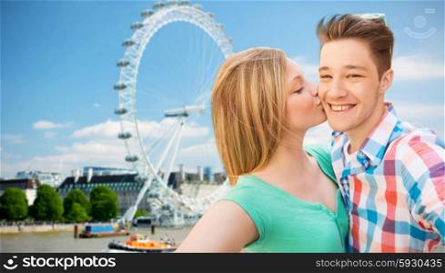 travel, vacation, technology and friendship concept - happy couple taking selfie over london ferry wheel background