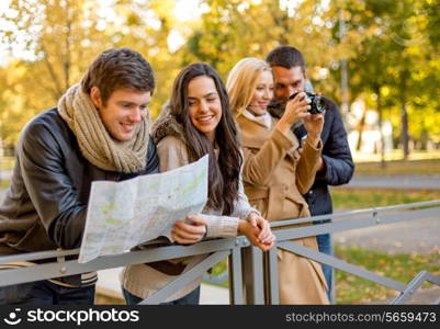 travel, vacation, technology, tourism and friendship concept - group of smiling friends with digital photo camera and map in city park