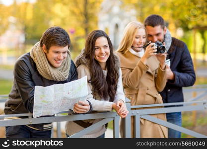 travel, vacation, technology, tourism and friendship concept - group of smiling friends with digital photo camera and map in city park