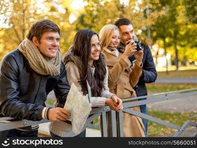 travel, vacation, technology, tourism and friendship concept - group of smiling friends with digital photo camera and map in city park