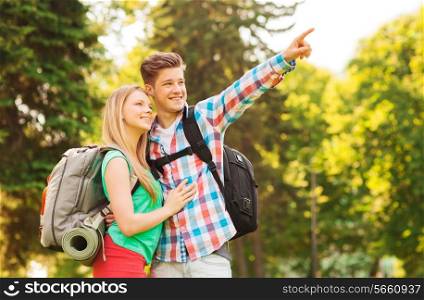 travel, vacation, tourism and friendship concept - smiling couple with backpacks pointing finger in nature