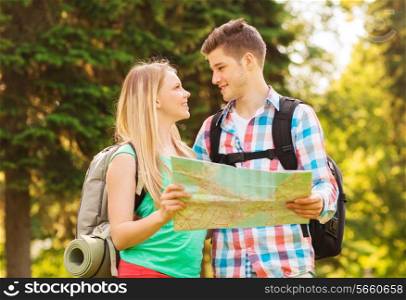 travel, vacation, tourism and friendship concept - smiling couple with map and backpacks looking at each other in forest