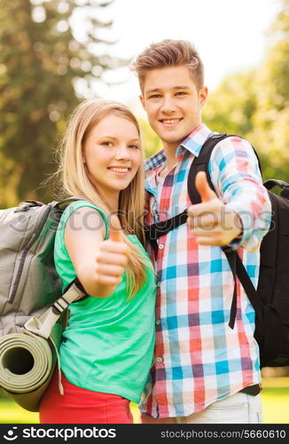 travel, vacation, tourism, gesture and friendship concept - smiling couple with backpacks showing thumbs up in nature