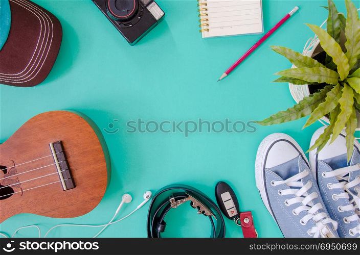 Traveler accessories. Shoes, , ukulele, pencils and notebooks and phone on the green background.