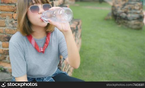 Traveler Asian woman drinking water while relax after spending holiday trip at Ayutthaya, Thailand, female enjoy her journey at amazing landmark in traditional city.