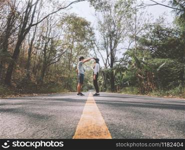 Traveler couple hold hands walking on country road amid trees. Happy couple enjoying free time while travelling.