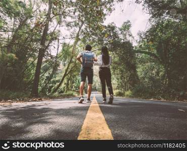 Traveler couple hold hands walking on country road amid trees. Happy couple enjoying free time while traveling.