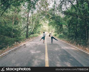 Traveler couple hold hands walking on forest road amid lush trees. Happy couple enjoying free time while traveling.