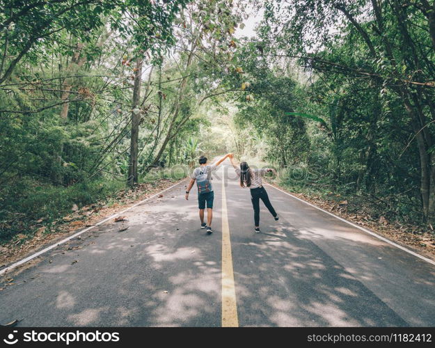 Traveler couple hold hands walking on forest road amid lush trees. Happy couple enjoying free time while traveling.