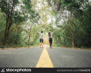 Traveler couple hold hands walking on roadway amid lush trees. Happy couple enjoying free time while traveling.