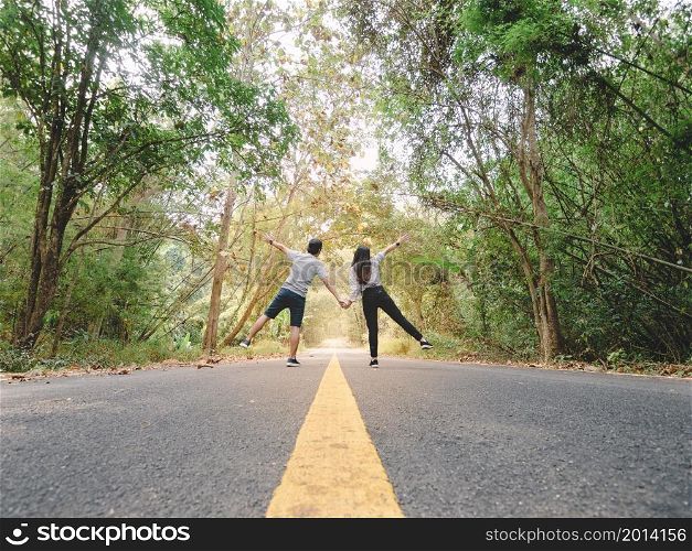 Traveler couple hold hands walking on roadway amid lush trees. Happy couple with open arms.