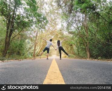Traveler couple hold hands walking on roadway amid lush trees. Happy couple with open arms.