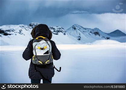 Traveler enjoying winter landscape, rear view of person standing among snows and wondering beautiful lands on snowy mountains, extreme travel to Iceland