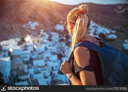 Traveler girl enjoying mountainous village view in bright sun light, many nice little white houses built on the mountain cliff, interesting summer adventure, touristic place, active lifestyle