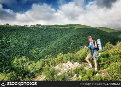 Traveler girl in the mountains, standing on the top of mount and showing by hands a good mood, active summer time, with interest discovering wild nature