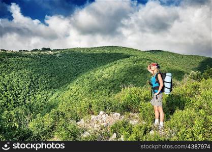 Traveler girl in the mountains, standing on the top of the mount and enjoying amazing landscape, active summer time, with interest discovering wild nature