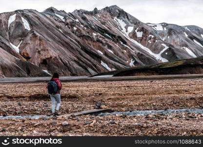 Traveler hiking at Landmannalaugar surreal nature landscape in highland of Iceland, Nordic, Europe. Beautiful colorful snow mountain terrain famous for summer trekking adventure and outdoor walking.