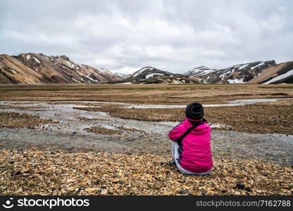 Traveler hiking at Landmannalaugar surreal nature landscape in highland of Iceland, Nordic, Europe. Beautiful colorful snow mountain terrain famous for summer trekking adventure and outdoor walking.