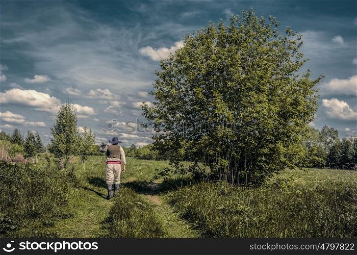 Traveler in old clothes with a knapsack on an abandoned country road. Toned