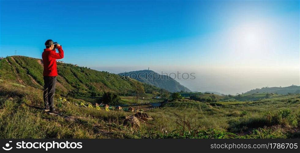 traveler looking in binoculars enjoying view above clouds during hiking trip