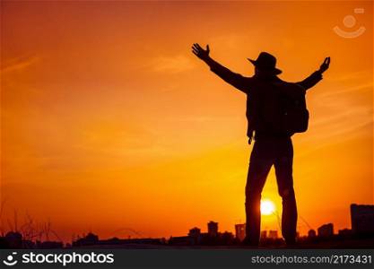 Traveler silhouette of man looking on sunset sky celebrating enjoying freedom, victory, success. Business concept and hands up. Orange toning filter. Lifestyle Travel Outdoor Background. Kiev, Ukraine. Traveler silhouette enjoying freedom, victory, success.