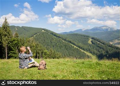 Traveler sits on mountain hill and looking through binocular. Travel and hiking concept