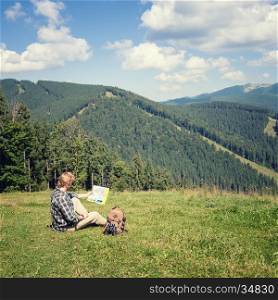 Traveler sitting on the alpine meadow and looking at the map