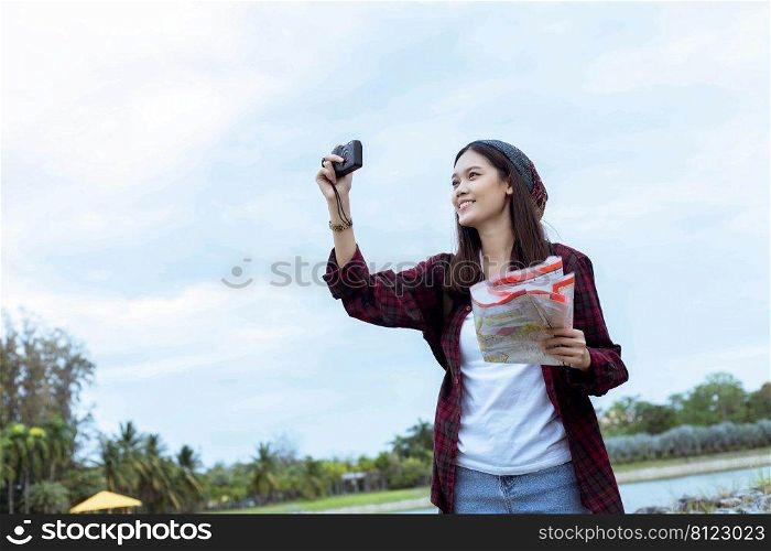 traveler, tourist Asian woman, carrying a backpack, smiling happily and looking at the camera to record a photo. and holding a map in the midst of nature