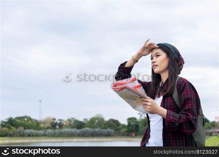 traveler, tourist Asian woman, carrying a backpack, smiling happily and looking at the camera to record a photo. and holding a map in the midst of nature