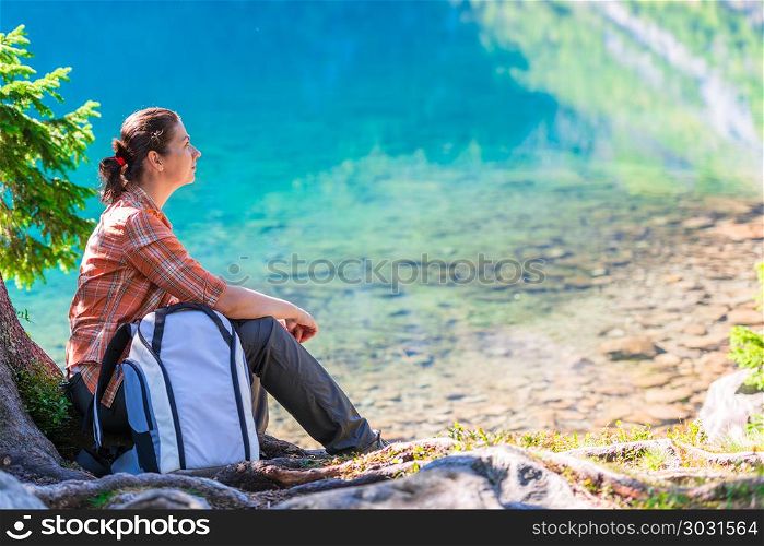 traveler with a backpack sits by the lake Morskie Oko in the Tat. traveler with a backpack sits by the lake Morskie Oko in the Tatra Mountains and admires