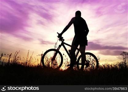 traveler with bike stopped on field at sunset time