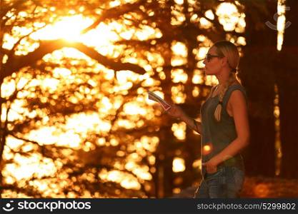 Traveler woman in the forest enjoying sunset, pretty girl standing in the woods with map in hand and searching right dirrection, active summer adventure