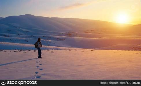 Traveler woman in the mountains enjoying beautiful sunset view, active winter holidays, amazing wintertime adventure