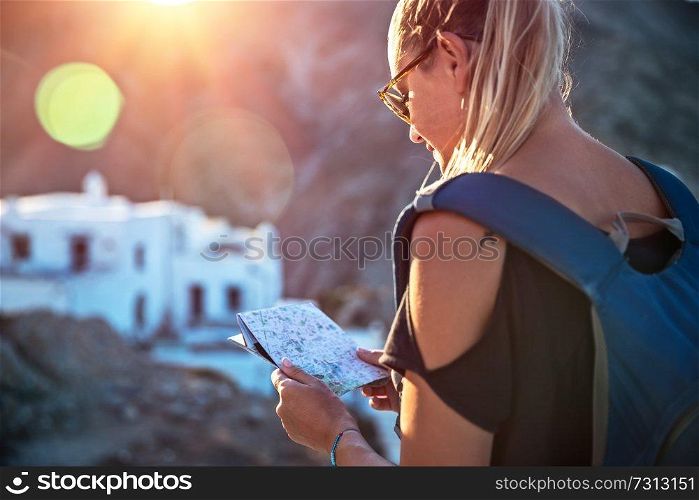 Traveler woman in trip to high mountins, pretty blond girl with map in hands and backpack searching the right way, enjoying view of mountainous city, active summer vacation