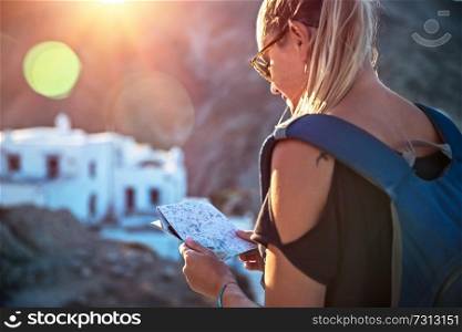 Traveler woman in trip to high mountins, pretty blond girl with map in hands and backpack searching the right way, enjoying view of mountainous city, active summer vacation