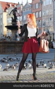 Traveler woman red haired fashion girl with smart phone outdoors in european city, old town Gdansk Neptune fountain in the background, Poland Europe