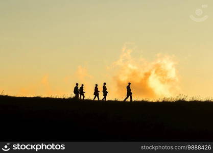 Travelers silhouettes against the orange light of sunset on the mountains.