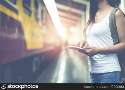 Travelers young woman with backpack looking hold tablet at the train station. Tourism day concept.