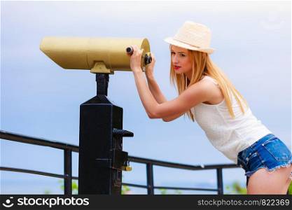 Traveling, adventure, vacation concept. Woman tourist wearing sun hat looking through telescope into the distance. Woman tourist with sun hat looking through telescope