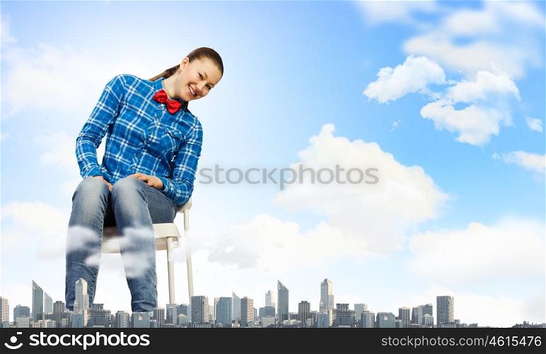 Traveling concept. Young giant woman sitting on chair above modern city
