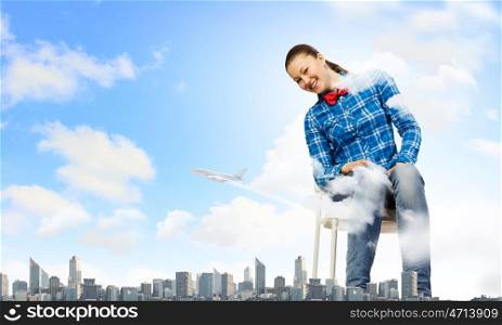 Traveling concept. Young giant woman sitting on chair above modern city